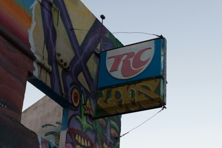 Blaues RC Cola (Royal Crown Cola) Werbeschild hängt an einer farbenfrohen Graffiti-Wand – urbane Streetart und Retro-Außenwerbung