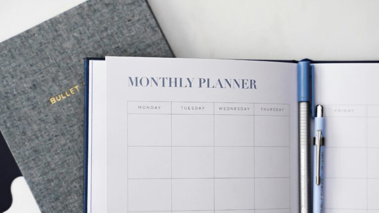 Aufgeklapptes Bullet Journal mit leerer Monthly Planner Seite neben einem blauen Stift – Produktivitätsplanung und Zeitmanagement mit analogen Hilfsmitteln