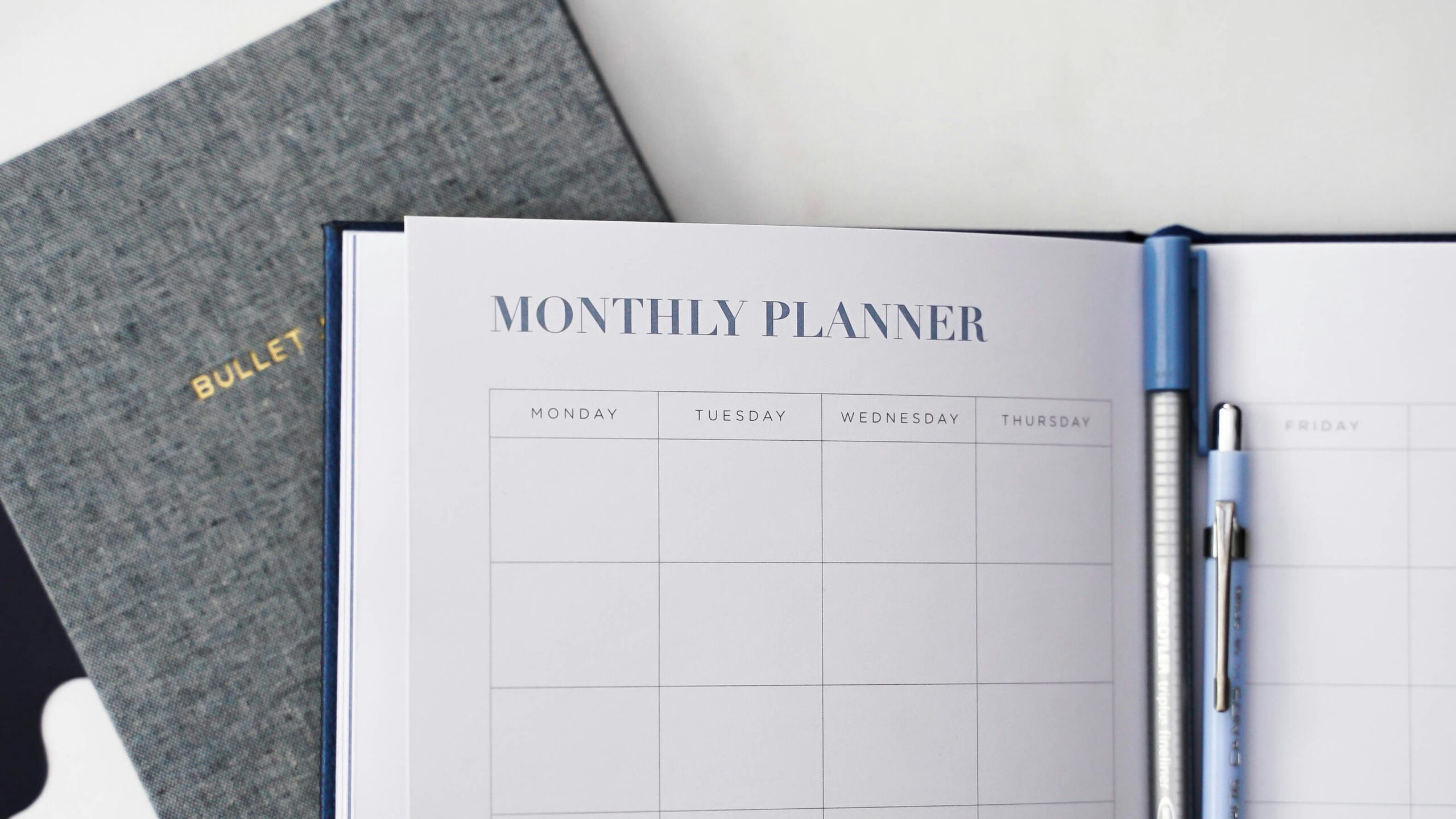 Aufgeklapptes Bullet Journal mit leerer Monthly Planner Seite neben einem blauen Stift – Produktivitätsplanung und Zeitmanagement mit analogen Hilfsmitteln