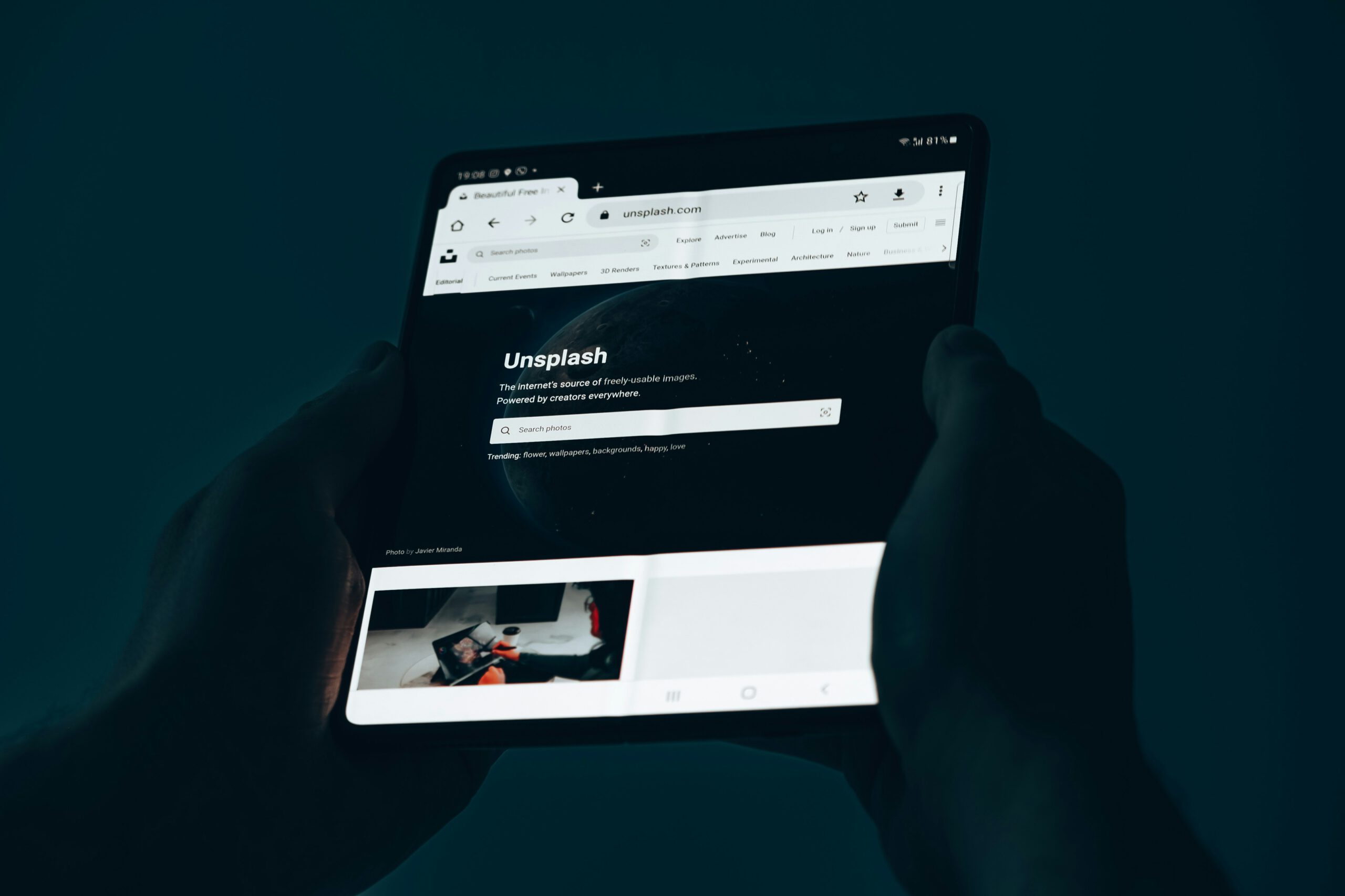 Hand hält ein Tablet mit geöffneter Unsplash-Website in dunkler Umgebung – kostenlose Stock-Fotografie Plattform für professionellen Webdesign und Content-Marketing
