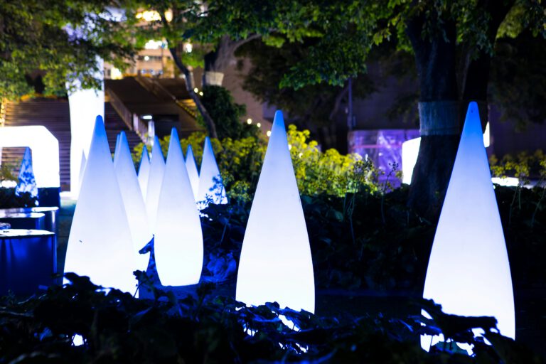 Leuchtende weiße Kegel-Lichtinstallationen in einem beleuchteten Garten bei Nacht mit Bäumen und blauem Lichtakzent – moderne Outdoor-Kunst und Lichtdesign